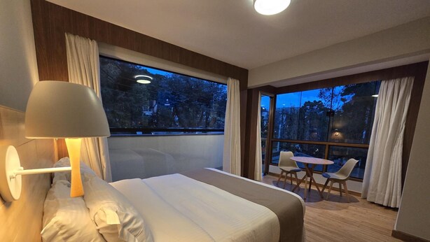 A hotel room with a large bed, a desk, and a view of the outdoors. - La Brume Pousada (Campos do Jordão)