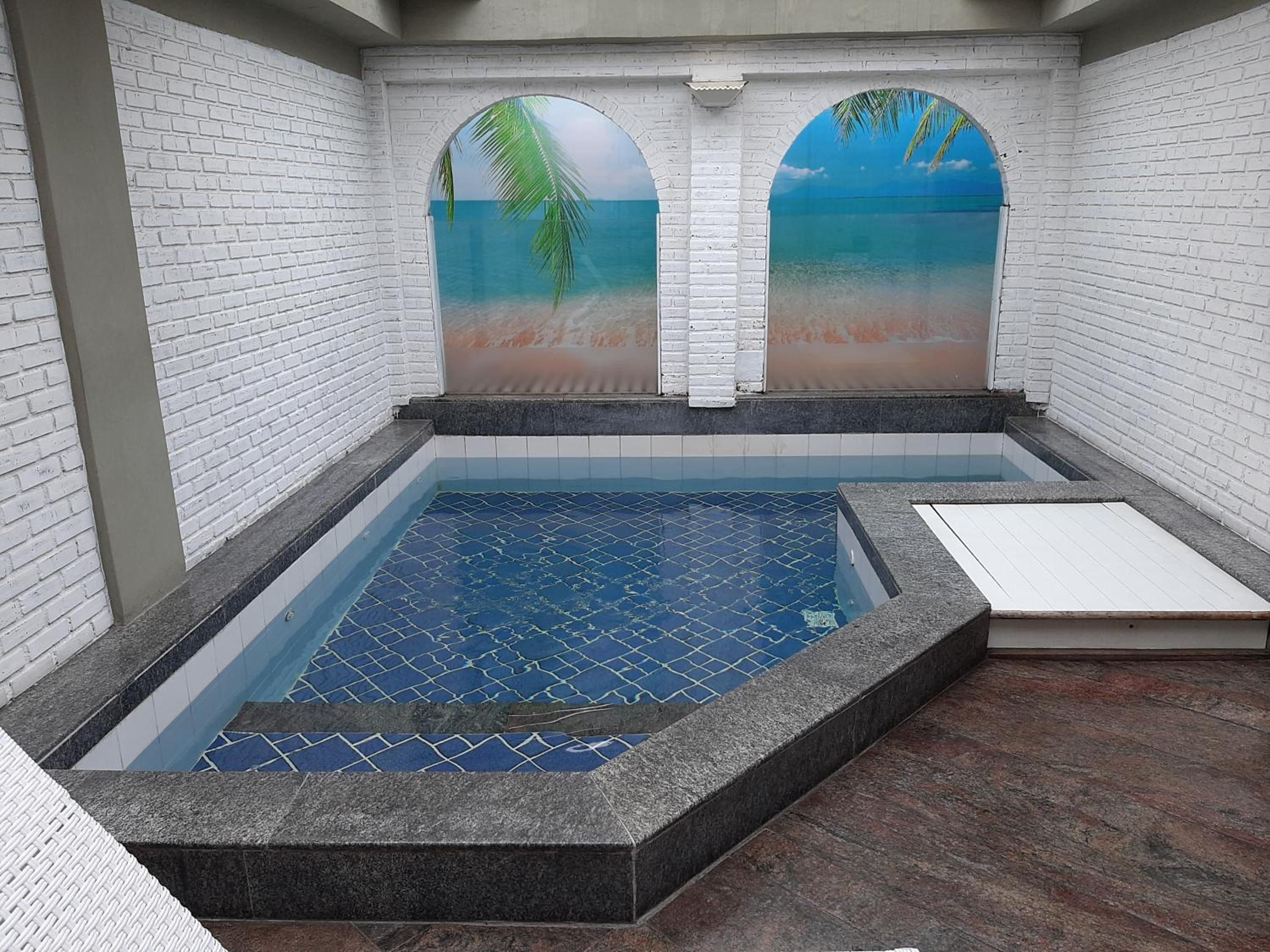 A swimming pool with a tiled floor and a view of a beach through an arched window.