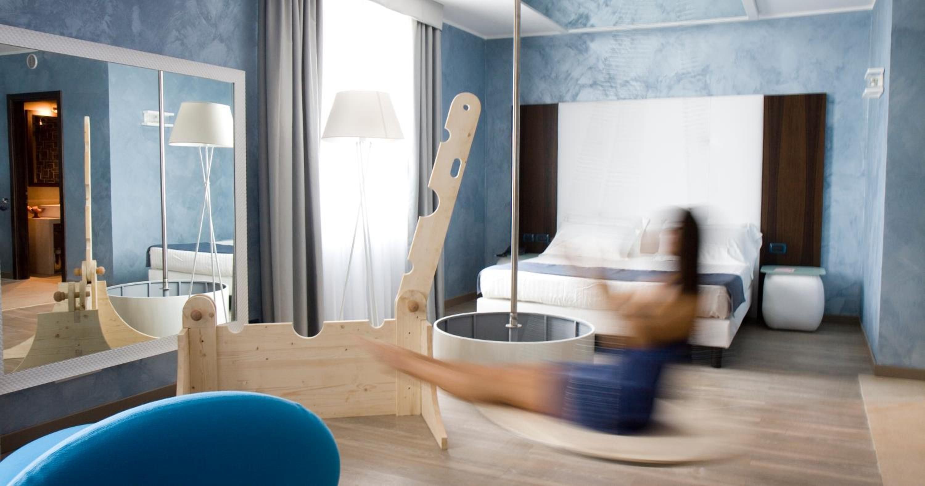 Ein modernes Hotelzimmer mit einem großen Bett, einem Schaukelstuhl aus Holz, einem runden Tisch und einer blauen Badewanne.