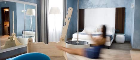 Ett modernt hotellrum med en stor säng, en gungstol i trä, ett runt bord och ett blått badkar.