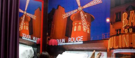 A hotel room with a bed, a window with curtains, and a wall mural of a windmill.