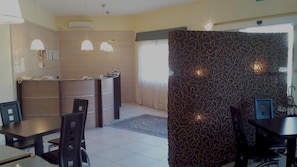Habitación de hotel con zona de comedor, mostrador de recepción y separador decorativo.