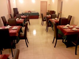 Un comedor con varias mesas dispuestas para el servicio, sillas alrededor y una mesa de buffet al fondo.
