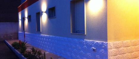 A building with exterior lighting, a window with blinds, and a planter with cacti.