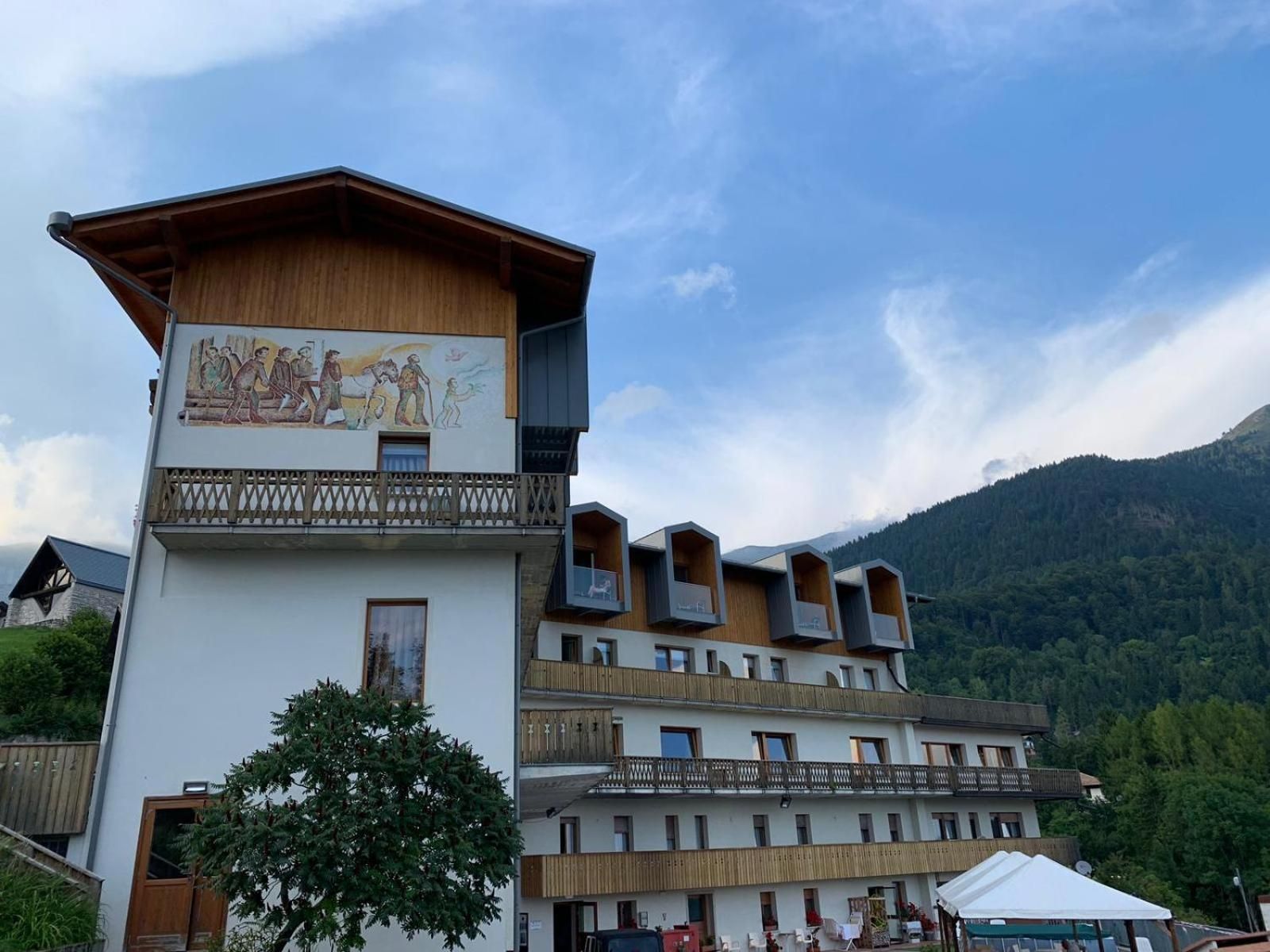 Un edificio de varios pisos con fachada de madera, un balcón con barandilla de celosía y un mural que representa una escena histórica.