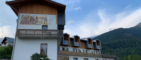 Un edificio de varios pisos con fachada de madera, un balcón con barandilla de celosía y un mural que representa una escena histórica.