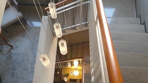 A staircase with a wooden handrail and white railings, leading to a room with a bed and hanging lights. - Albergo Baschera (Fagagna)