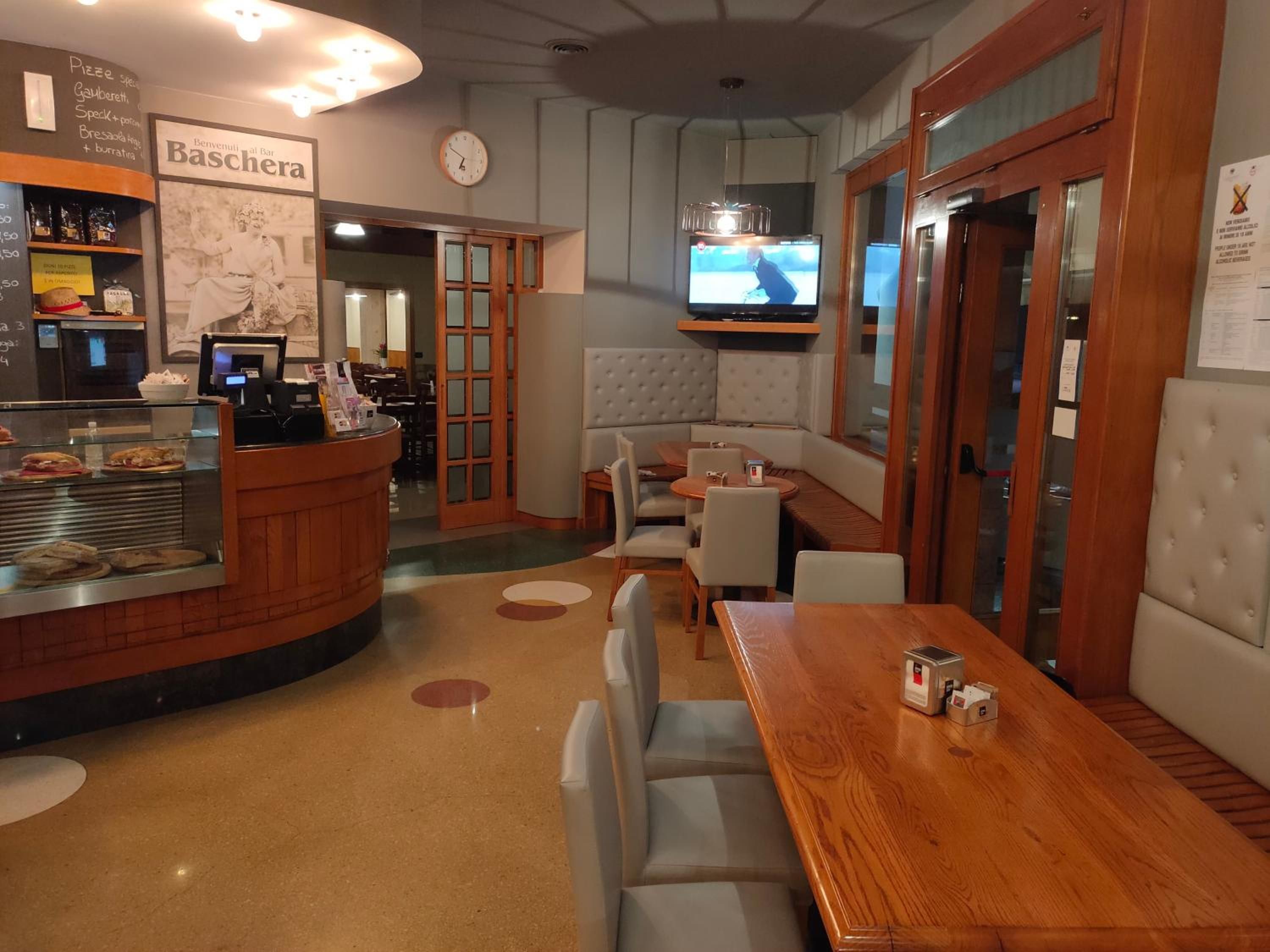 Interior de restaurante con mostrador, zona de asientos y televisión en la pared.