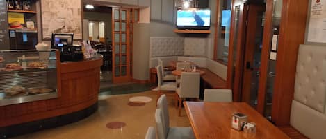 Interior de restaurante con mostrador, zona de asientos y televisión en la pared.