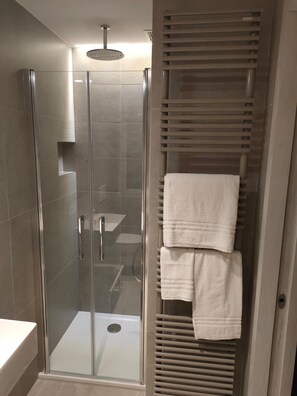 Ein modernes Badezimmer mit einer gläsernen Dusche, einem weißen Waschbecken und einem Handtuchhalter mit gefalteten Handtüchern.