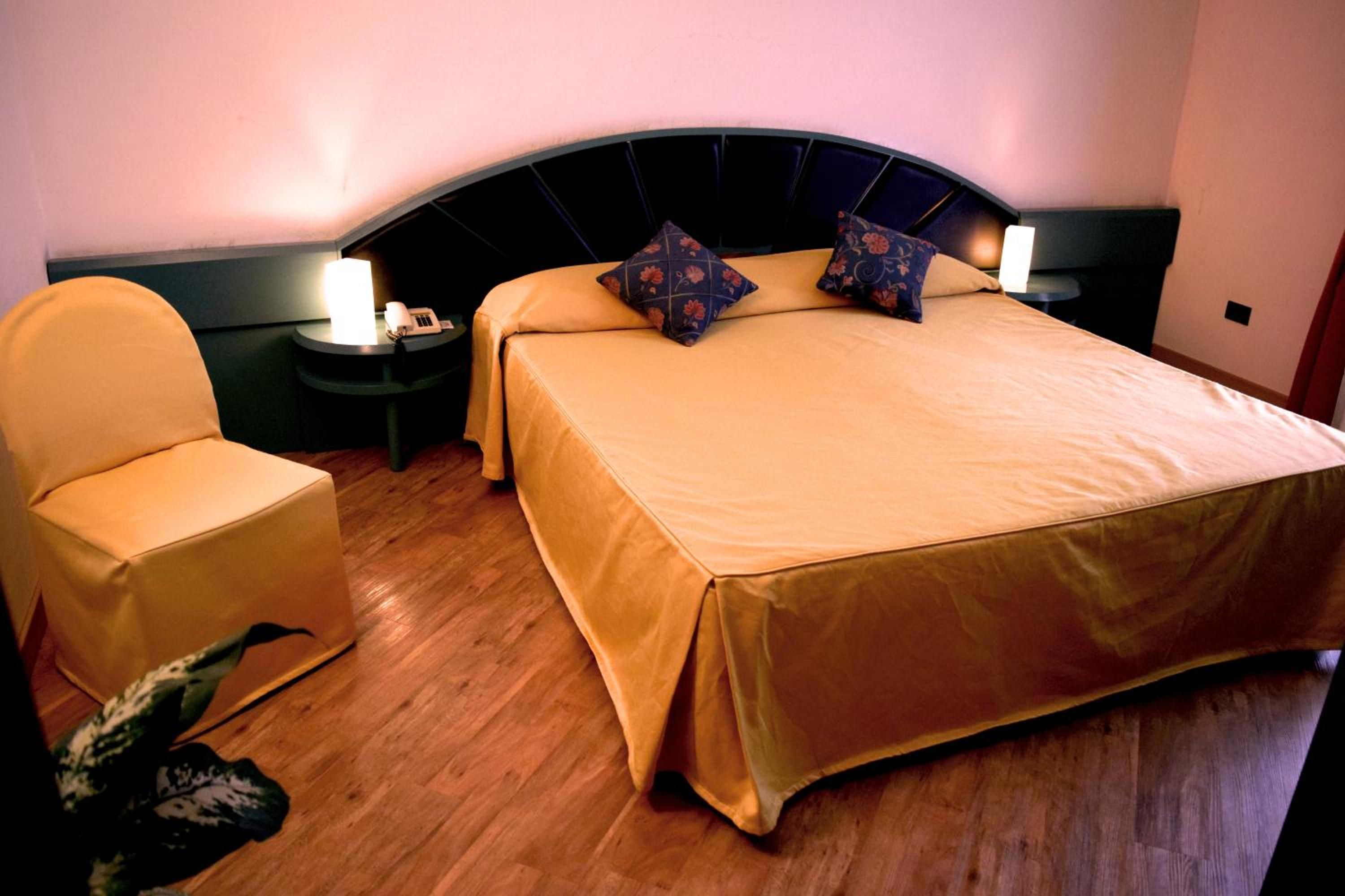 Una habitación de hotel con una cama, una silla, una mesita de noche y una lámpara.