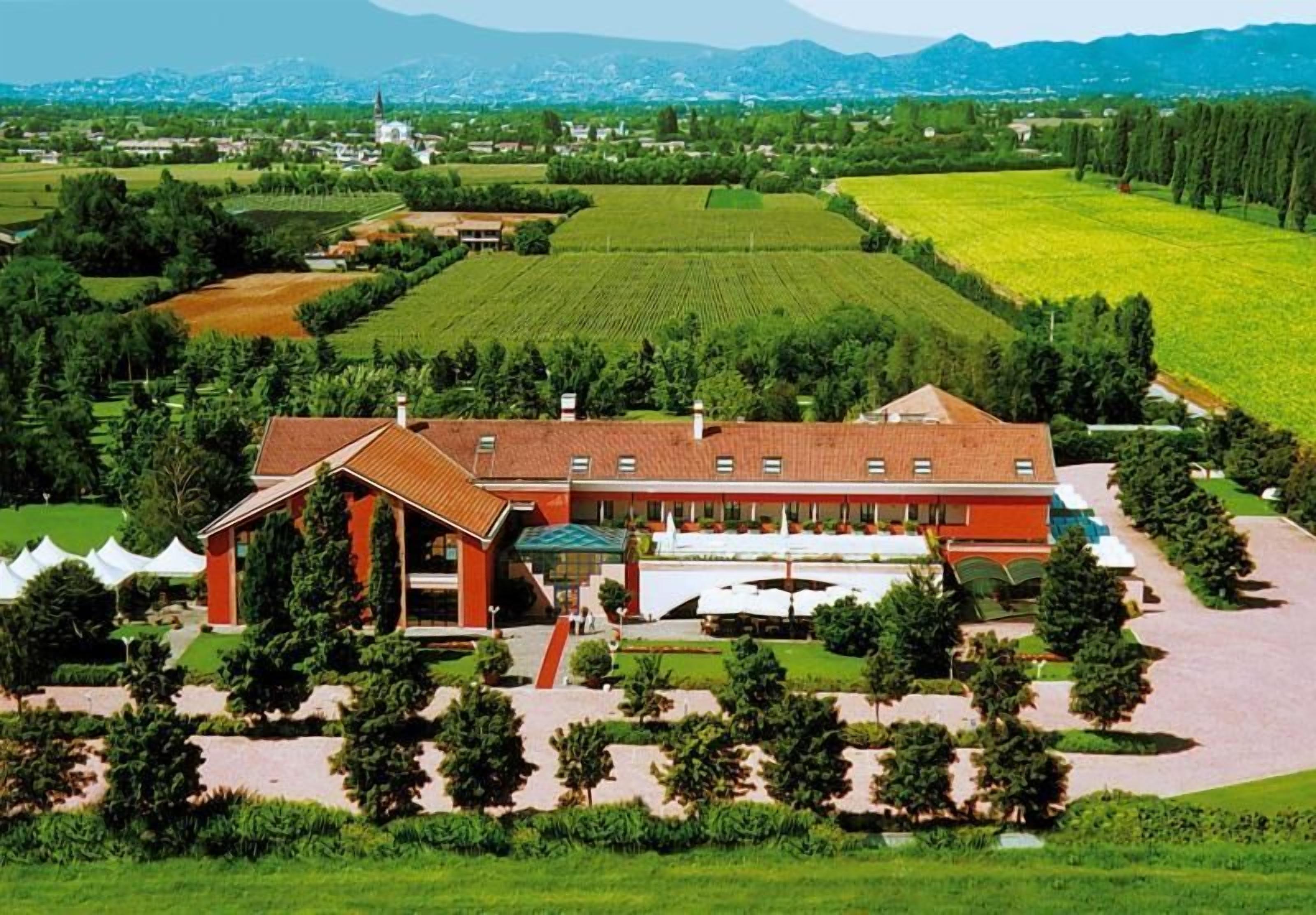 A large building with a red roof, surrounded by landscaped gardens and a vineyard.