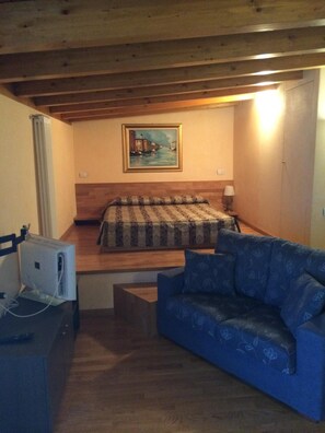 A bedroom with a bed, a blue sofa, a painting on the wall, and a radiator.