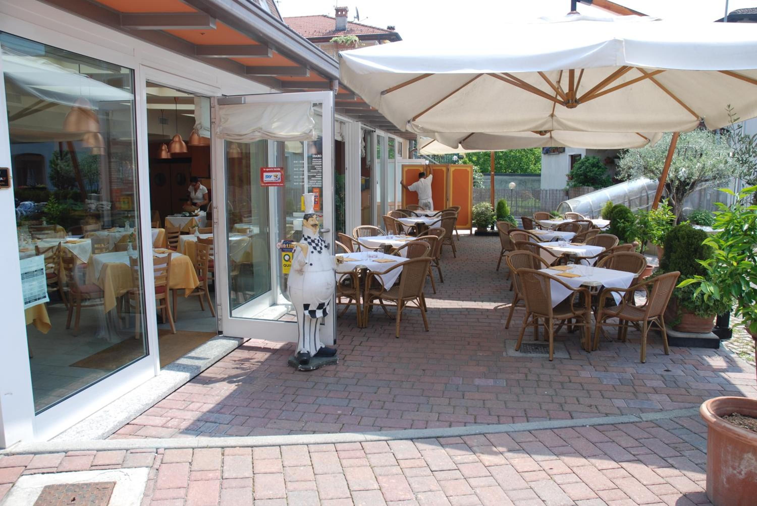 Un espace extérieur aménagé pour les repas, avec des tables et des chaises, un grand parasol et une entrée avec une porte vitrée.