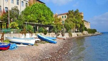 A pebbled beach with boats and a building with a balcony overlooking the sea.
