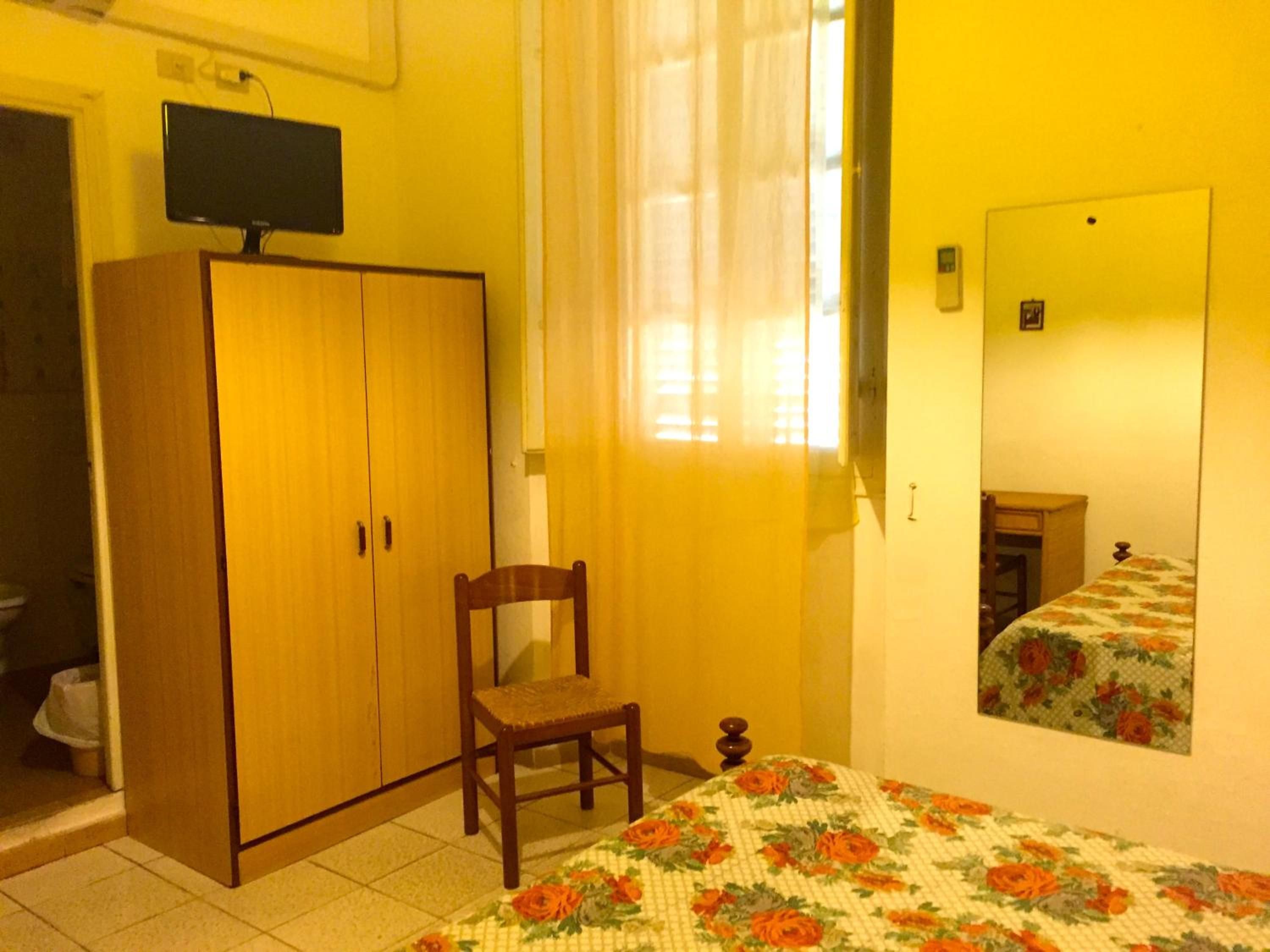 A room with a bed, a wooden wardrobe, a chair, a television on the wall, and a window with curtains.