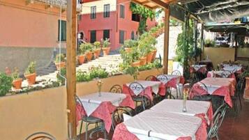 An outdoor seating area with tables and chairs, covered by a wooden pergola, and potted plants.