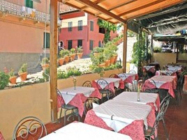 An outdoor seating area with tables and chairs, covered by a wooden pergola, and potted plants.
