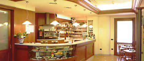Un bar de hotel con una barra curva, una máquina de café y una variedad de botellas. Hay sillas y mesas para que los huéspedes se sienten a comer.