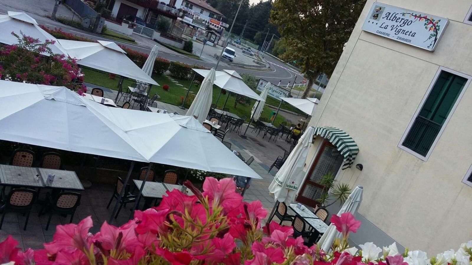 An outdoor seating area with umbrellas and tables, a building with a sign, and a road in the background.
