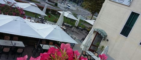 An outdoor seating area with umbrellas and tables, a building with a sign, and a road in the background.