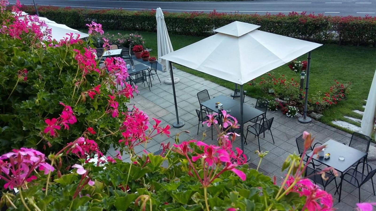 Una terrazza all'aperto con tavoli e sedie, circondata da piante fiorite e ombrelloni.