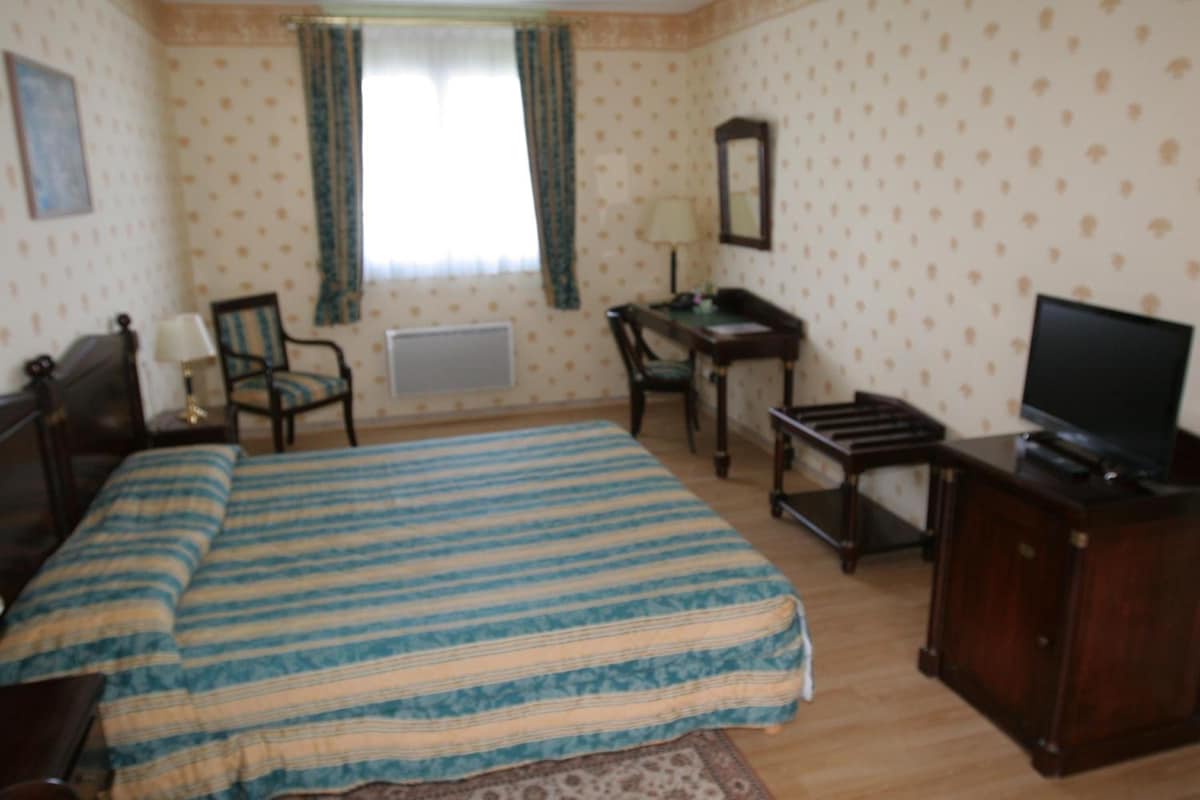 Habitación de hotel con cama, dos sillas, escritorio, televisor y ventana con cortinas.