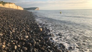 Una playa de guijarros con un acantilado a un lado y un mar tranquilo.