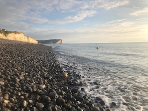 Una playa de guijarros con un acantilado a un lado y un mar tranquilo.