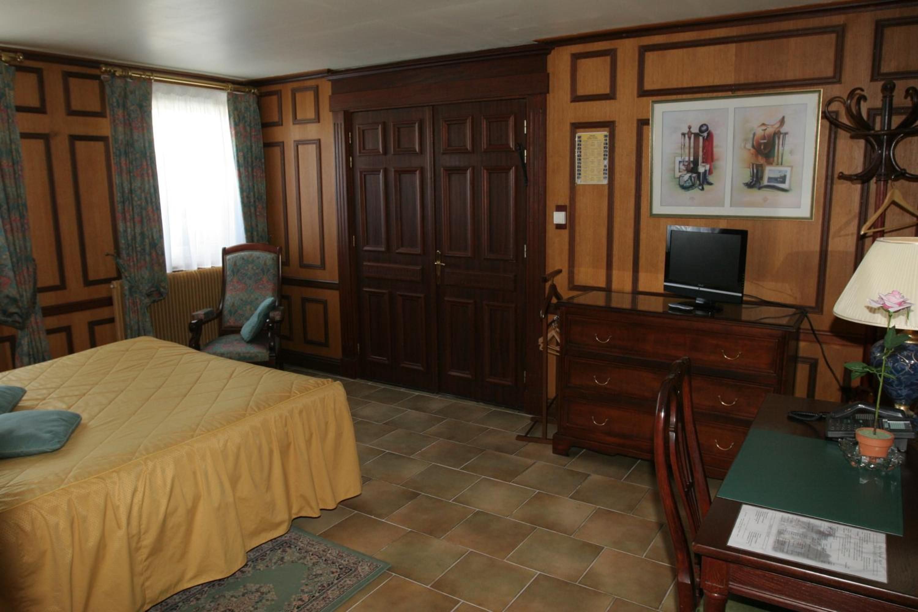 Een kamer met een bed, een stoel, een dressoir, een televisie en een ingelijst schilderij aan de muur.