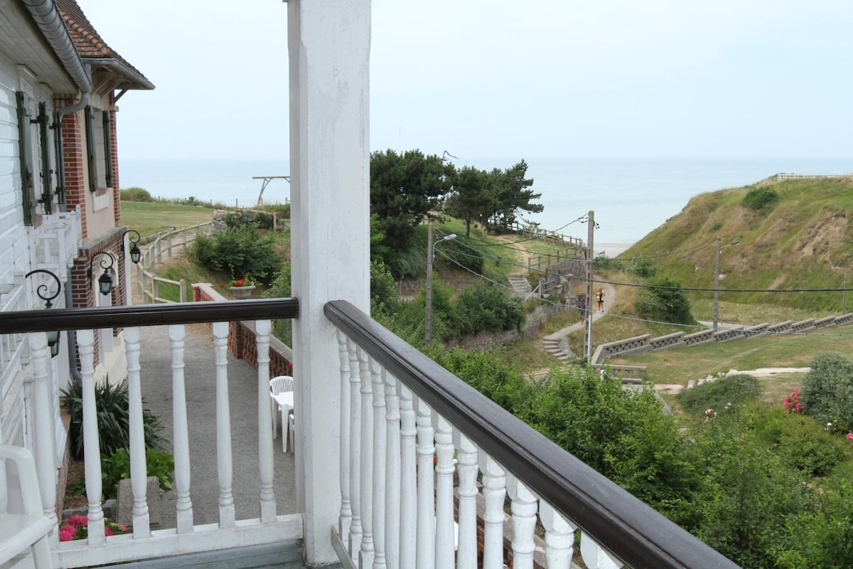 A balcony with a view of a coastal landscape, including a pathway and a hill.
