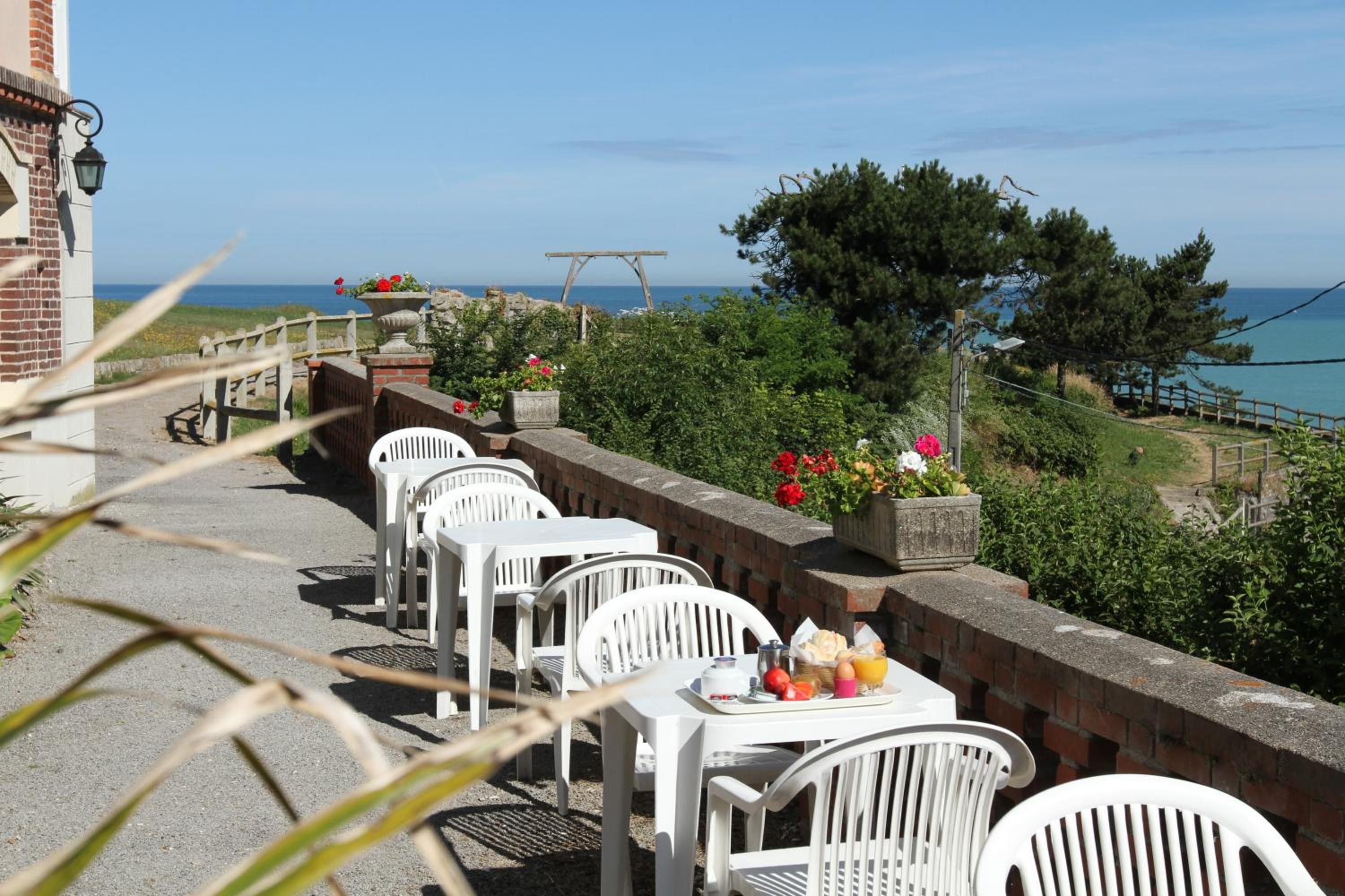 Una terraza frente al mar con sillas y mesas de plástico blanco, un muro de ladrillo y vistas al océano.