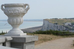 Un paysage côtier caractérisé par une falaise imposante, un bâtiment blanc et un vase décoratif.