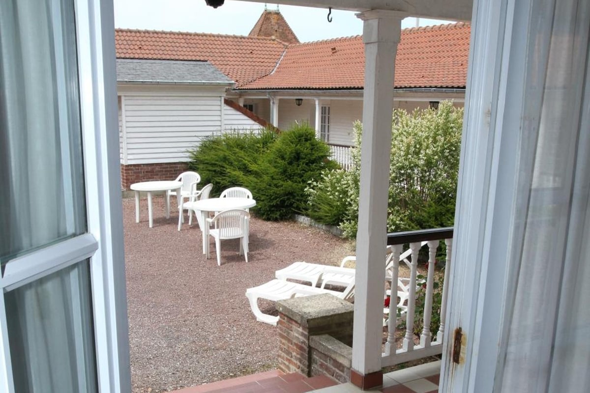 A view from a doorway onto a checkered outdoor patio with white furniture and a brick wall in the background.