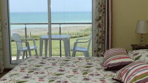 Una habitación con cama, una mesita, dos sillas, una lámpara y vista al mar.