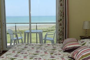Una habitación con cama, una mesita, dos sillas, una lámpara y vista al mar.