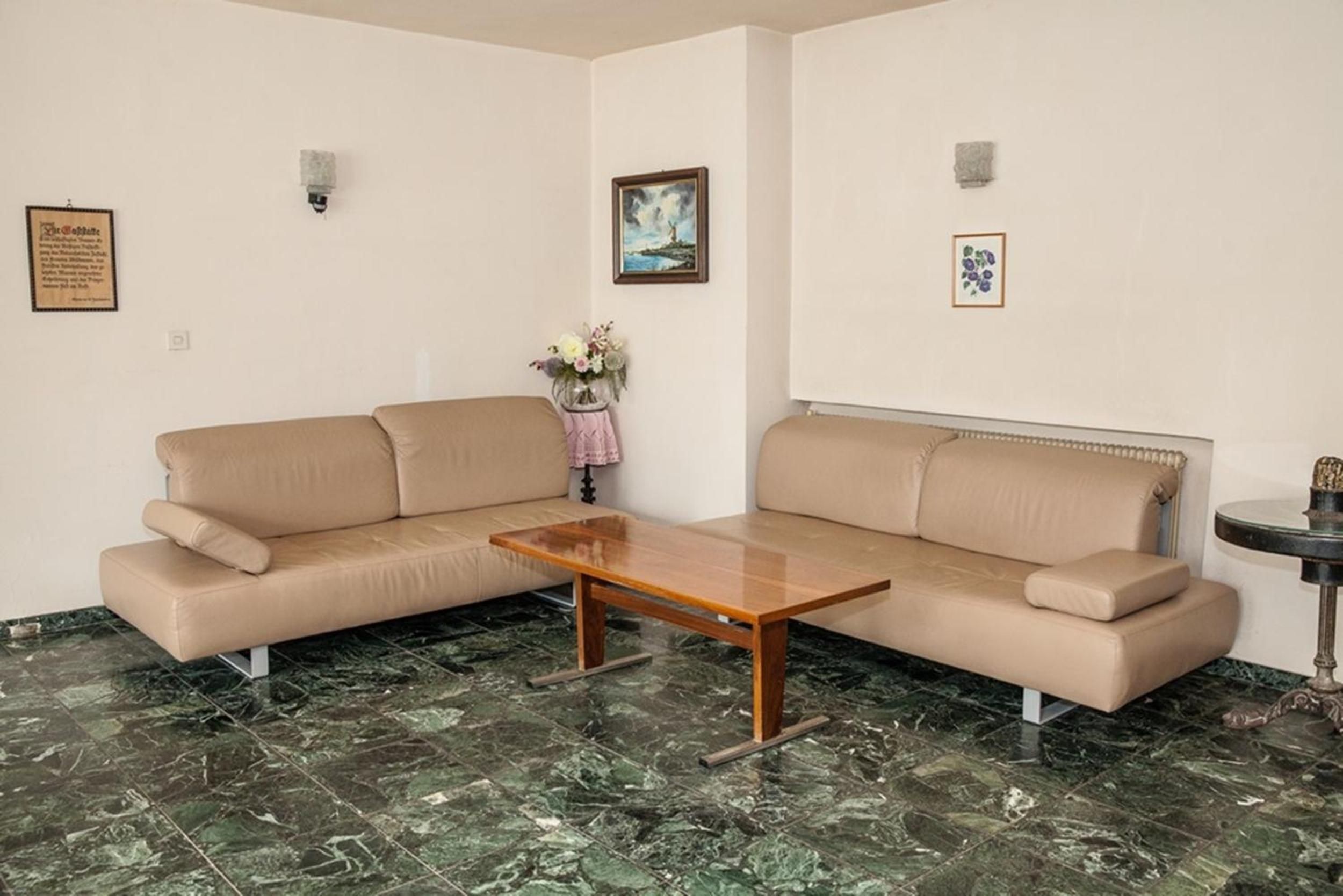 Ein Wohnzimmer mit einem beigen Sofa, einem Holztisch und einer Vase mit Blumen.
