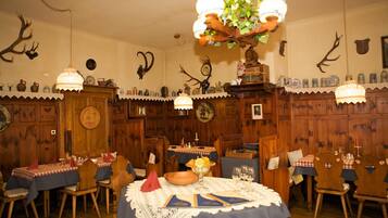 Ein Esszimmer mit Holzwänden, einer Kristallleuchtre und Geweihverzierungen.