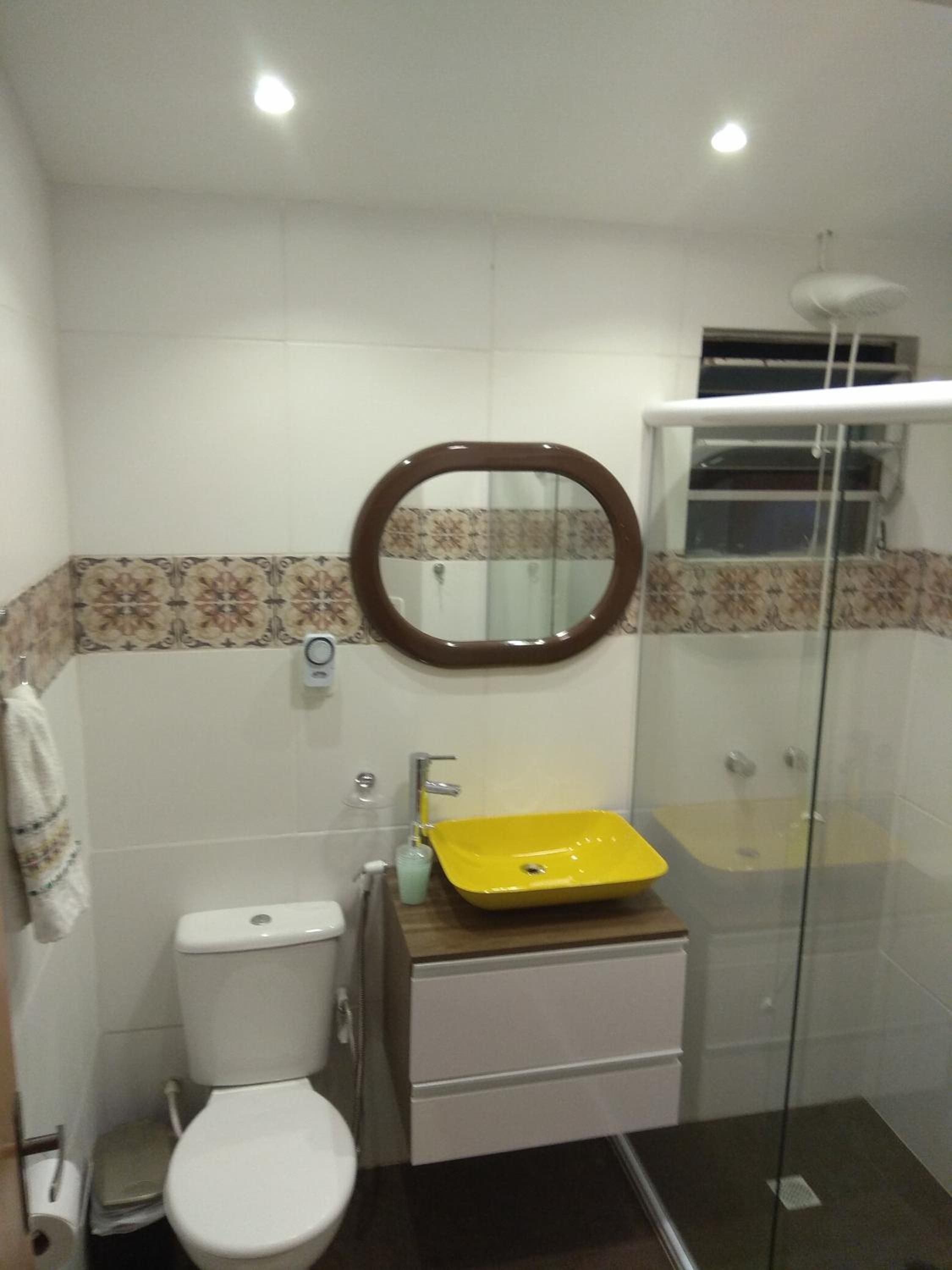 A bathroom with a toilet, a yellow sink, a mirror, and a glass shower enclosure.