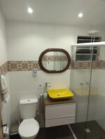 Casa de banho com sanita, uma pia amarela, espelho e cabine de duche em vidro.