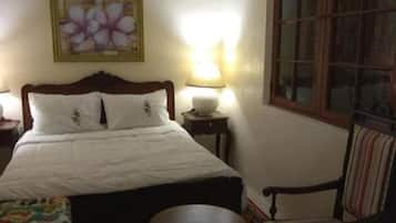 A bedroom with a bed, a chair, a small table, a lamp, a painting, and a window.