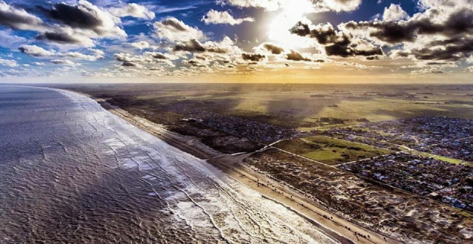 A coastal landscape with a beach, fields, and a town.