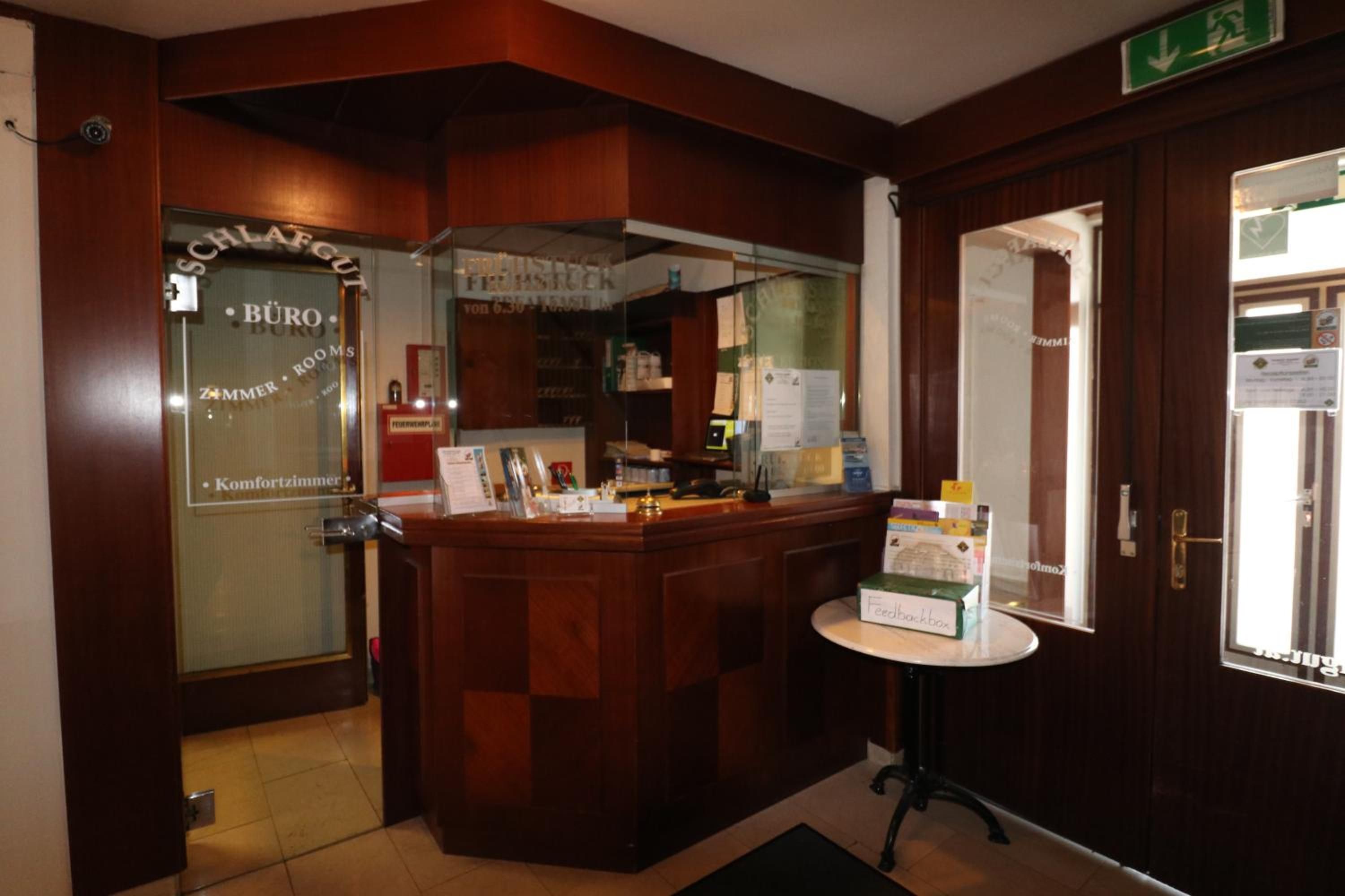 Ein Hotel-Rezeptionsbereich mit einem Holzbüro, einer Glastür mit Beschilderung und einem kleinen Tisch mit einer Kiste darauf.