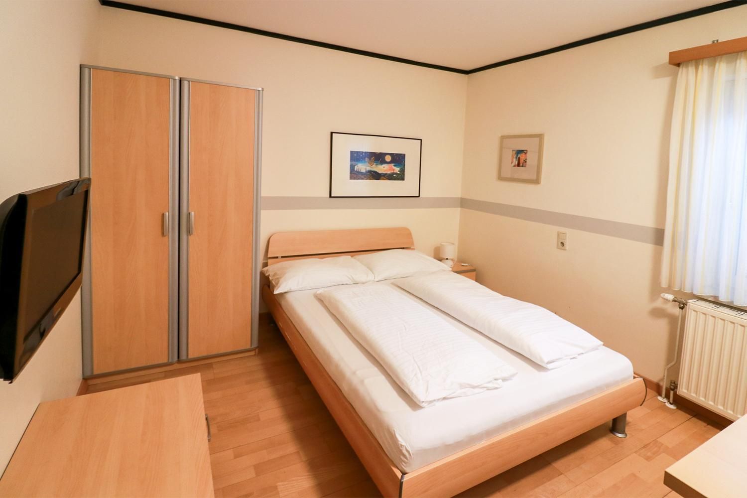 Ein Hotelzimmer mit Bett, Kleiderschrank, Nachttisch, Fernseher und einem Fenster mit Vorhängen.