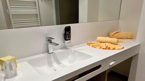 Un baño moderno con un lavamanos blanco, dispensador de jabón y toallas dobladas con esmero.