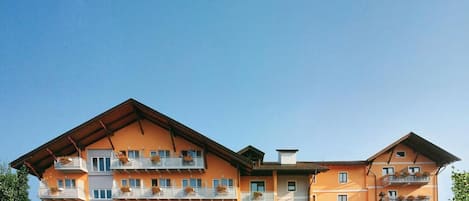 A multi-story hotel with a flat roof, balconies with flower boxes, and a covered entrance area.