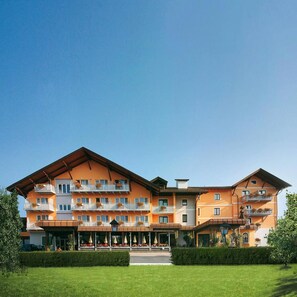 Un hotel de varios pisos con techo plano, balcones con jardineras y un área de entrada cubierta.