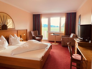 Habitación de hotel con cama, dos sillones, escritorio con televisor y ventana con vista al exterior.