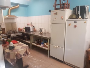 A compact kitchen with white cabinets, a stove, a refrigerator, and a table with a patterned tablecloth. - Hostel P33 (Tallinn)