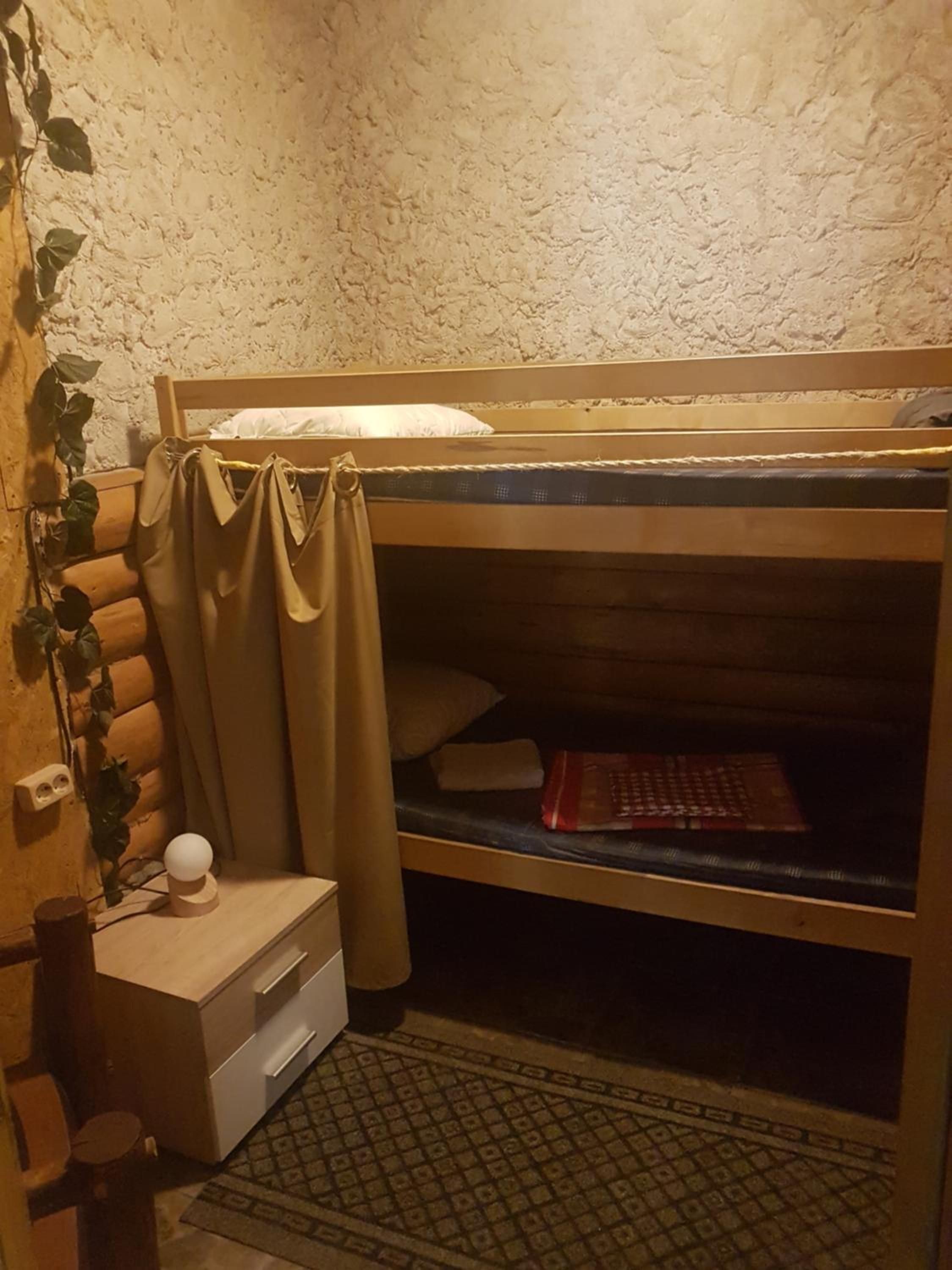 Una cama litera con cabecera, una mesita de noche con cajones, una lámpara pequeña y un enchufe en la pared.